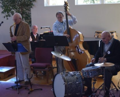 Four men on sax, piano, drums and bass are playing music.