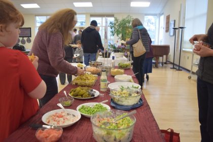 People helping themselves from a potluck table with side dishes and salads 2017-1-22